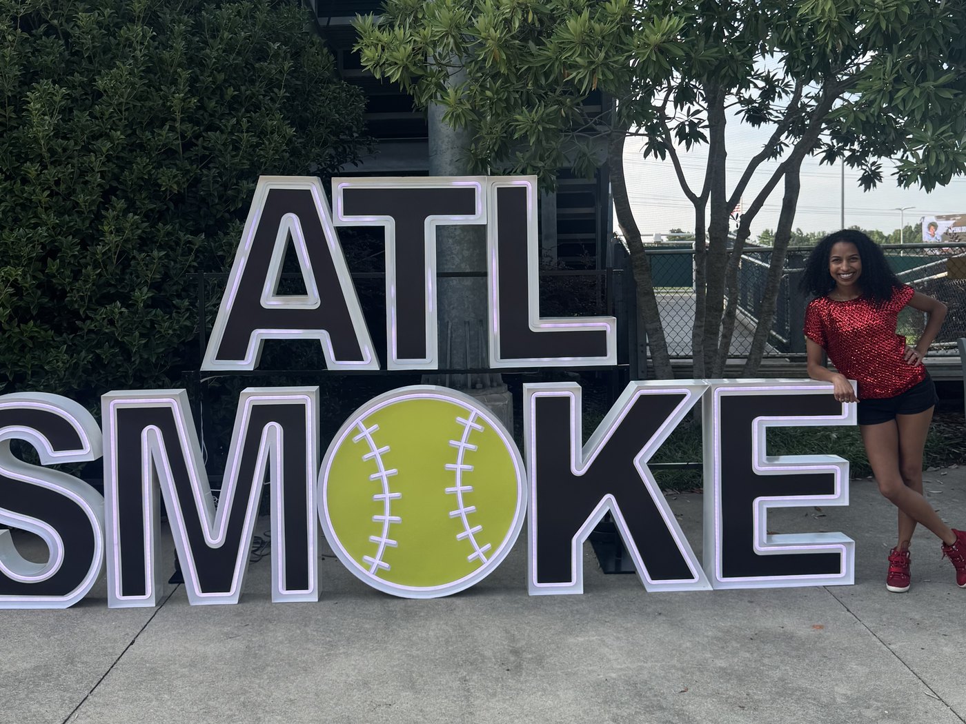Chelsea leaning on the lit-up ATL SMOKE sign at the ballpark