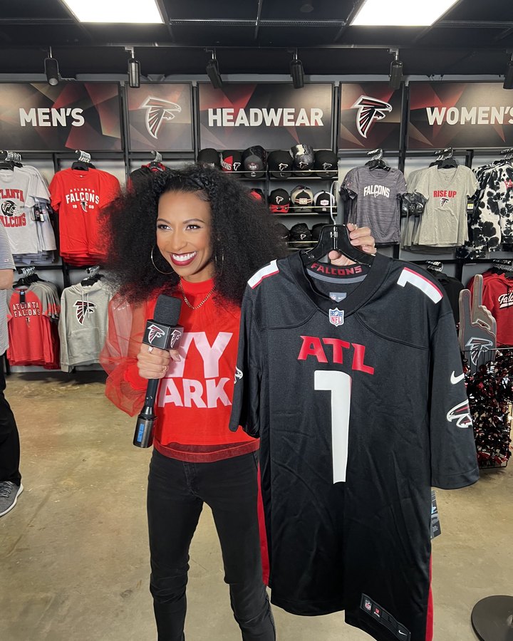 Chelsea holding up a Falcons jersey in the team store with a Falcons mic